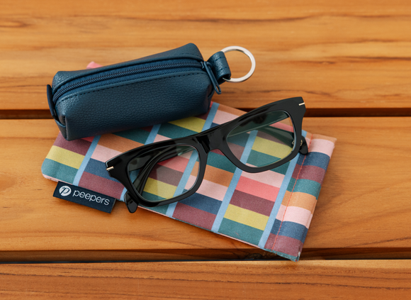 Black glasses on a colorful checkered cloth with a blue case on a wooden surface
