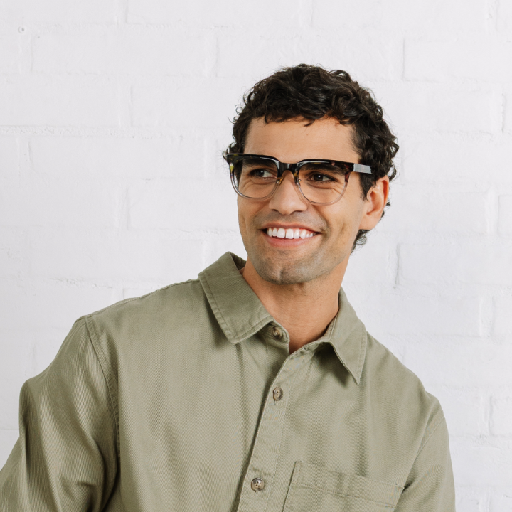 Man wearing glasses and a green shirt against a white brick wall