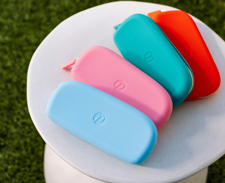 Four colorful silicone cases (blue, pink, turquoise, red) on a white surface with grass background.