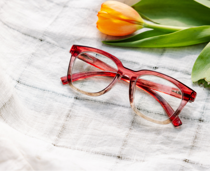 rose ombre eyeglasses on a textured white surface with a yellow tulip.