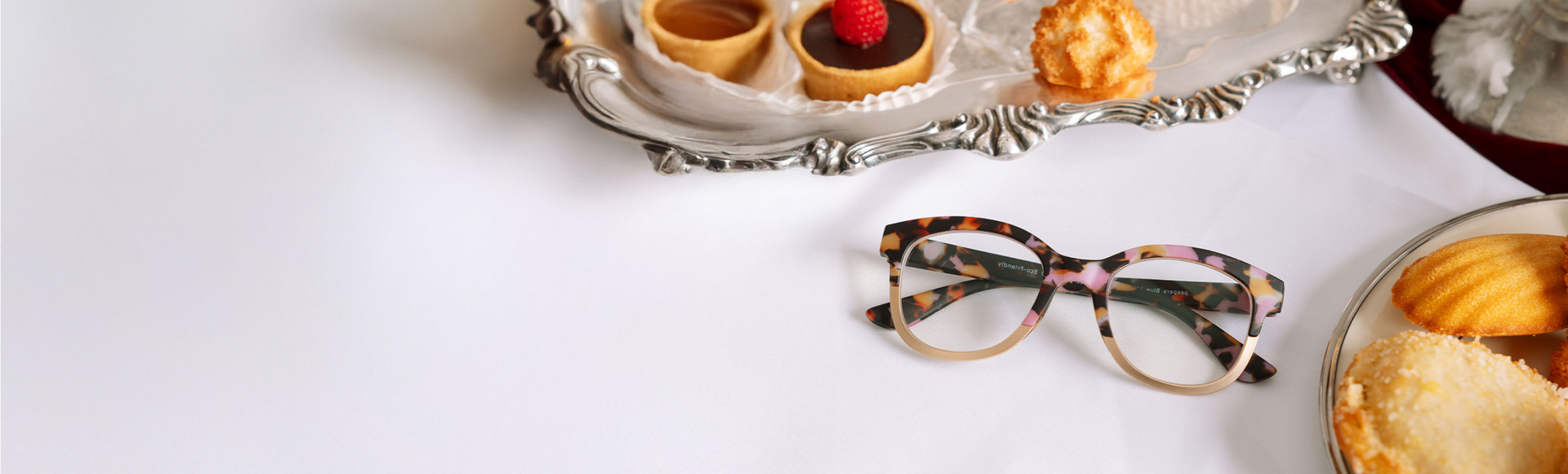 Tortoiseshell sunglasses on a white surface with pastries in the background