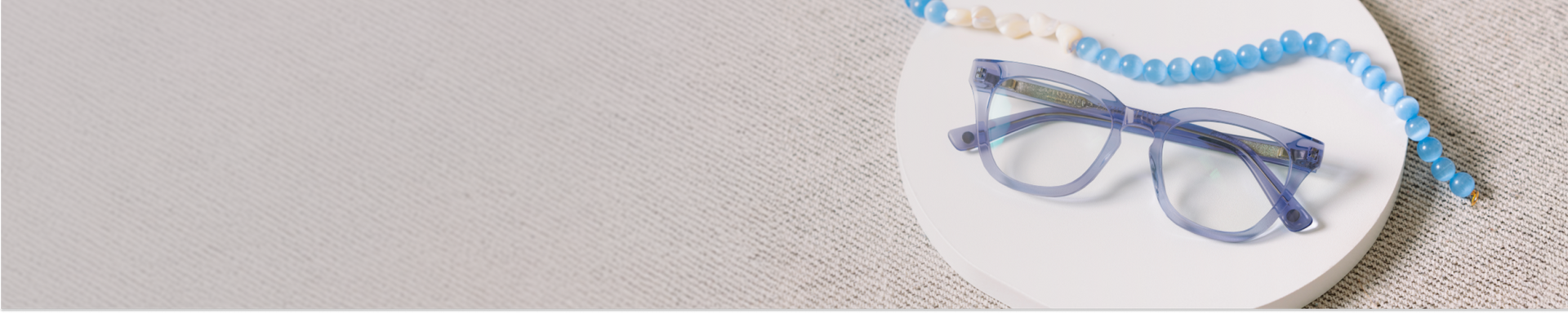 Blue eyeglasses on a white plate with blue beads on a beige background