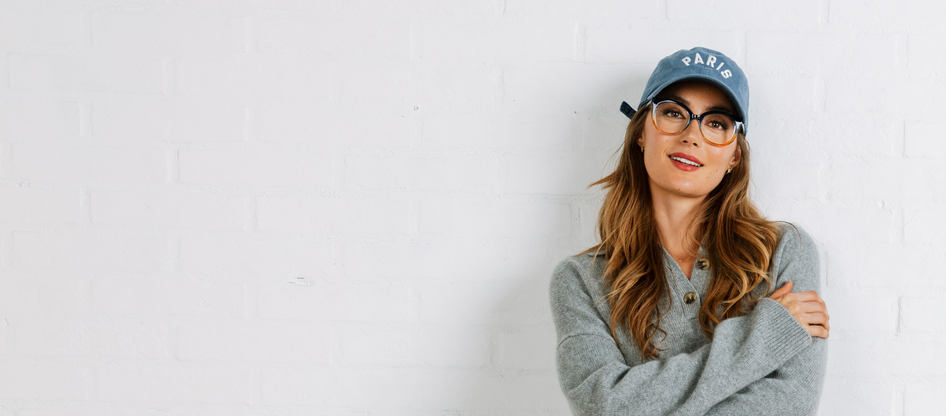 Woman wearing a gray sweater and blue cap with 'PARIS' text against a white background