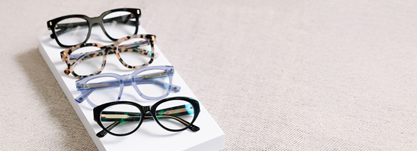 Four pairs of eyeglasses on a white rectangular platform with a light gray background