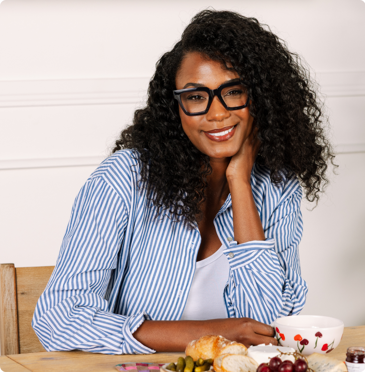 Woman sitting at a table with a plate of food, wearing glasses and a blue striped shirt.