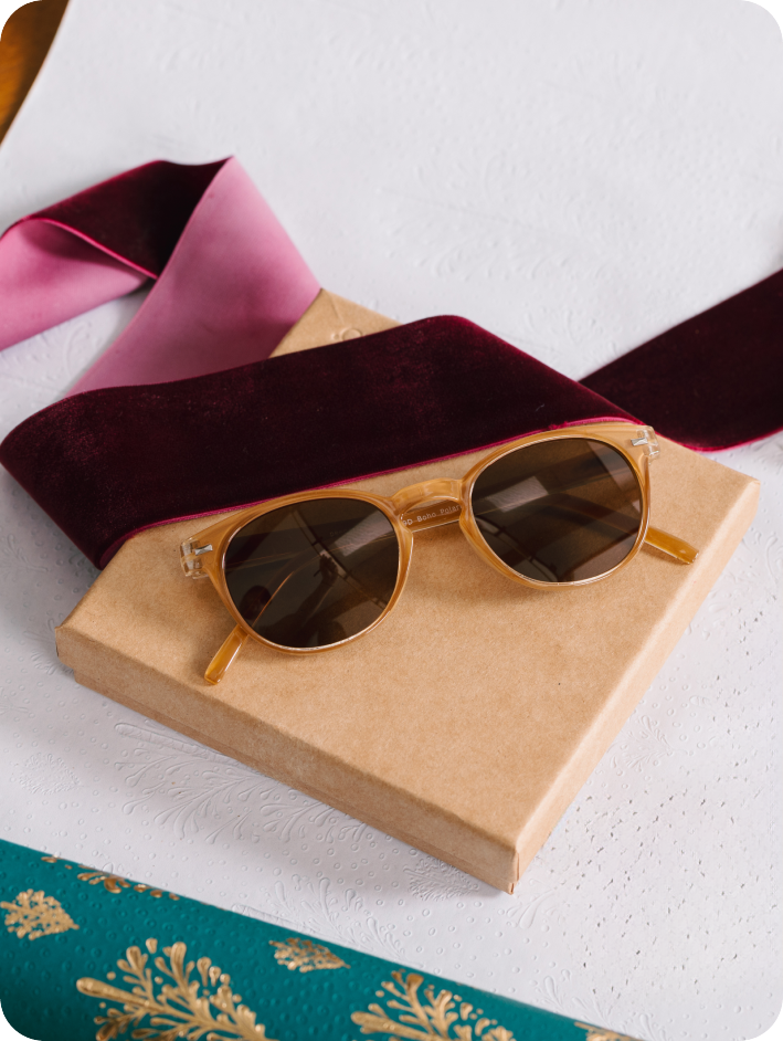 tan sunglasses on a beige box with pink and red ribbons on a white background