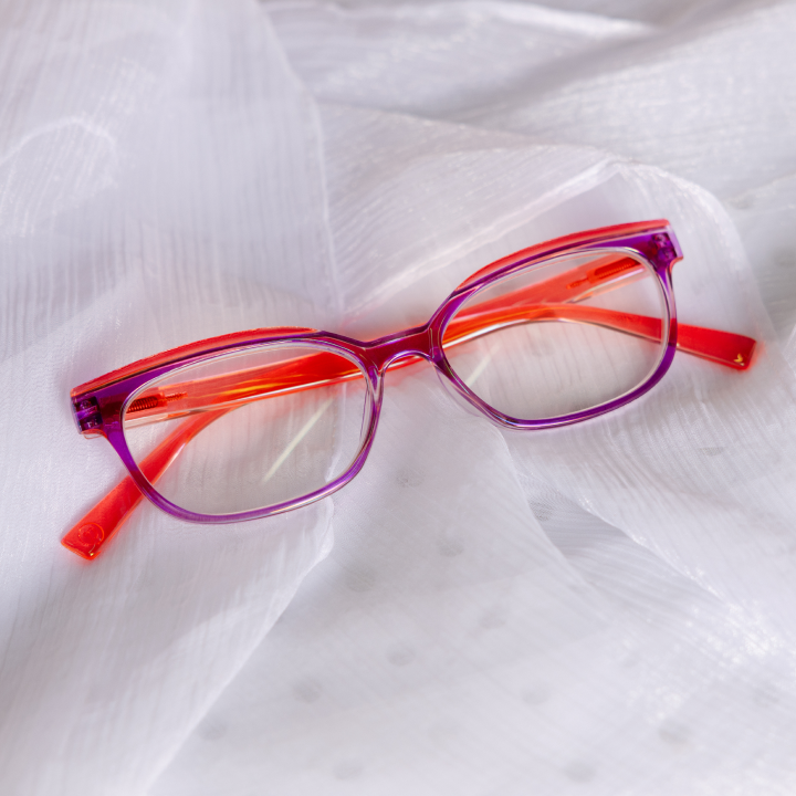 Pair of glasses with red and purple frame on a white fabric background