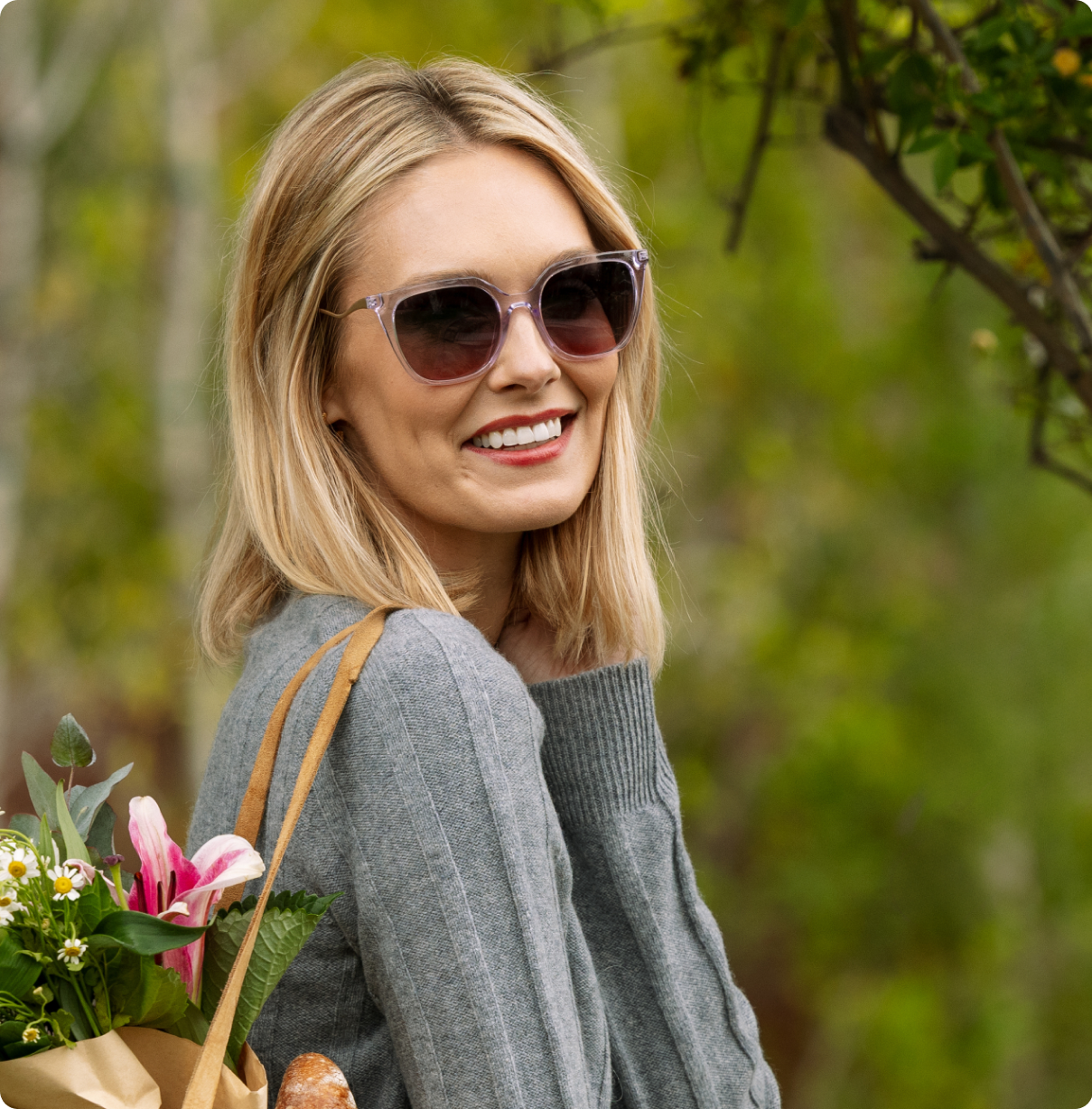 Woman wearing sunglasses and a gray sweater with a blurred green background