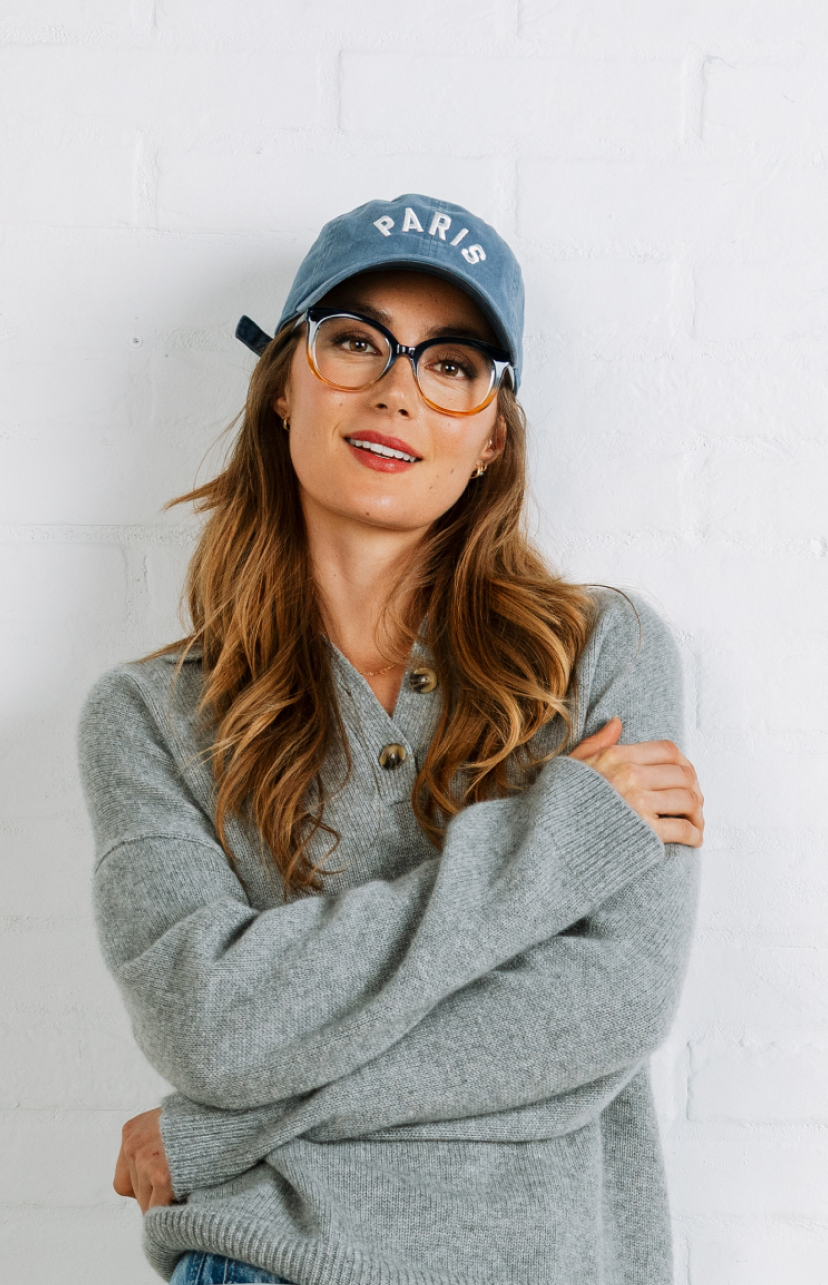 Woman wearing a gray sweater and blue cap with 'PARIS' text against a white background