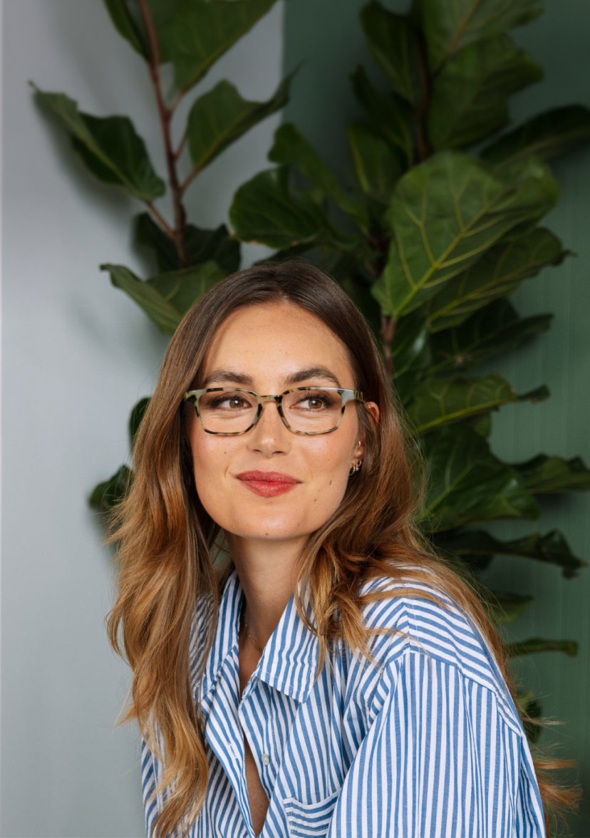 Woman wearing glasses and a striped shirt in a room with green walls and a plant.