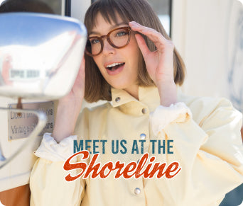 A woman with short brown hair and glasses smiles while touching her forehead, wearing a pale yellow jacket. A retro-style car mirror is visible on the left, and the text 'MEET US AT THE Shoreline' appears across the lower center.