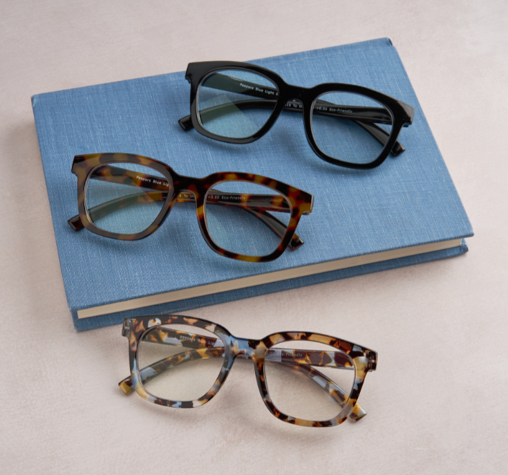 Three pairs of eyeglasses on a blue book with a light background