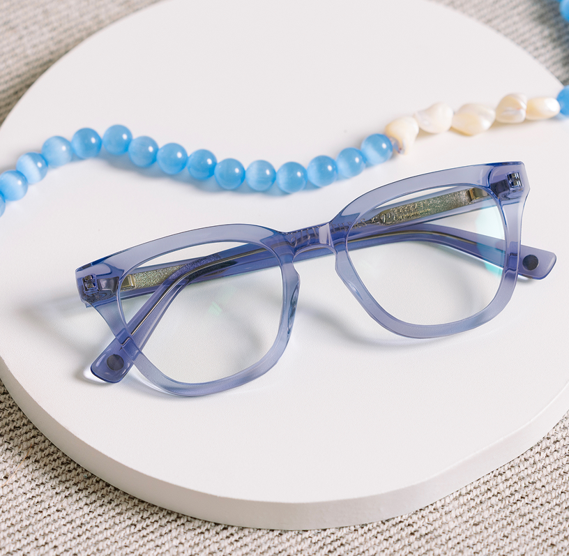 Blue eyeglasses on a white surface with a blue beaded necklace and pearls.
