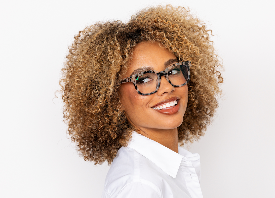 Woman with curly hair wearing glasses and a white shirt on a white background