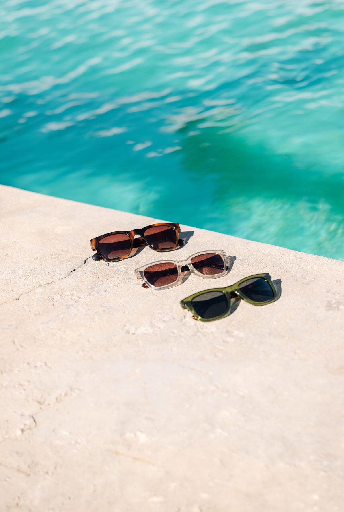Peepers sunglasses arranged on sunlit sand by the pool